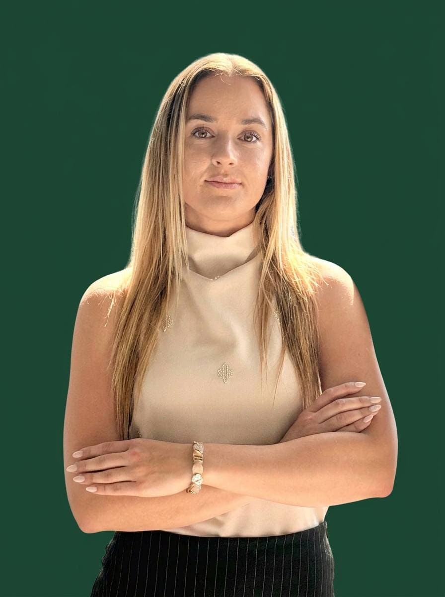Portrait of Laura Dunárová — blonde hair, arms crossed, cream mock-neck top with sparkling detail, on a deep green backdrop
